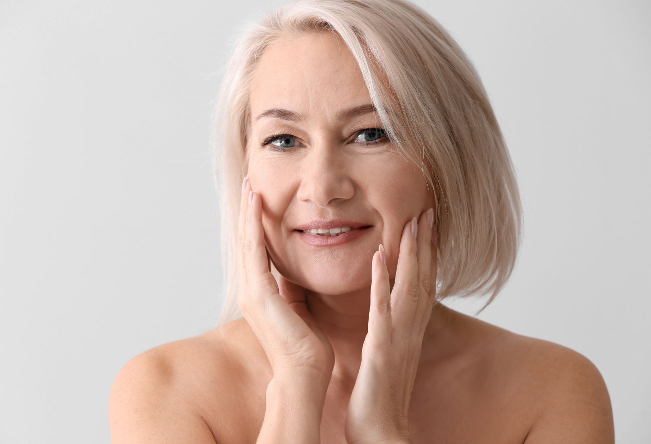 Mature woman touching smooth cheeks after plastic surgery recovery with HBOT.