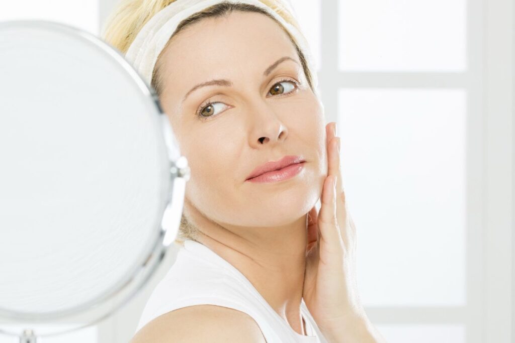 Woman examining her lips in the mirror, considering a lip filler touch-up to maintain volume and definition.