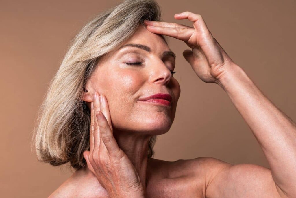 Confident older woman touching temples and jawline, highlighting five-year facial fat transfer volume retention and aging changes.