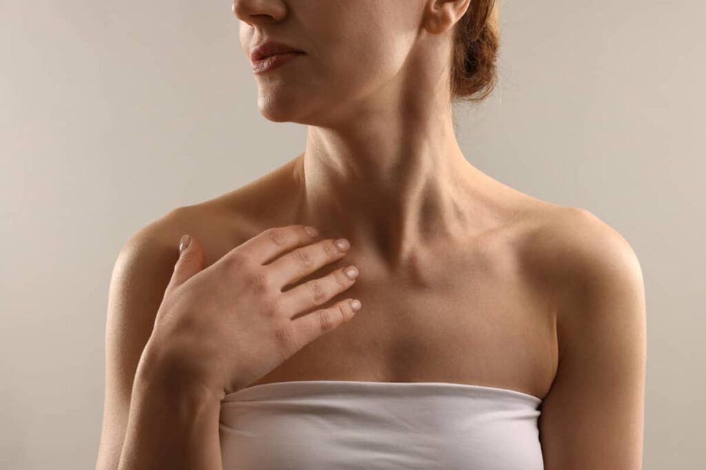 A woman in a white tube top looking to the side, showcasing her neck profile and collarbone area in soft lighting.