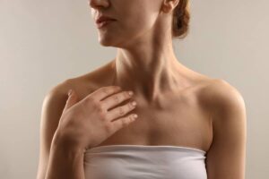 A woman in a white tube top looking to the side, showcasing her neck profile and collarbone area in soft lighting.