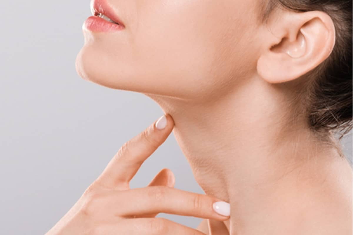 A close-up profile view of a woman's jawline and neck as she points her finger to the area below her chin to highlight the surgical site.