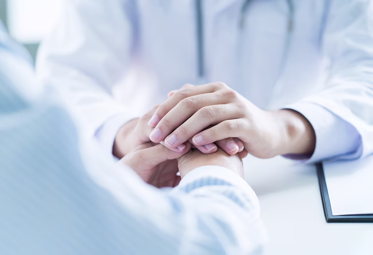 Doctor gently holding patient’s hands during post-operative consultation, symbolizing supportive recovery care in facial plastic surgery clinic